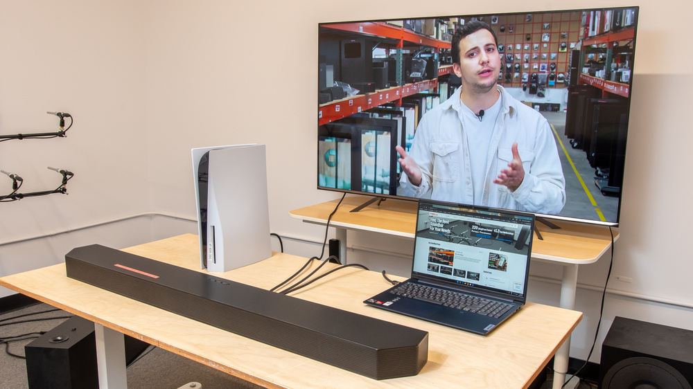 A soundbar connected to a TV with a PS5 and laptop on the side.