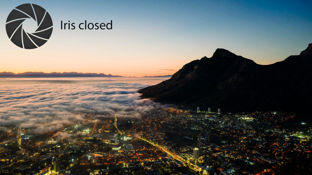 A panoramic shot of Cape Town at dusk, with an overlay indicating the projector's iris is closed. The black levels in dark areas are excellent, and the overall contrast is good.