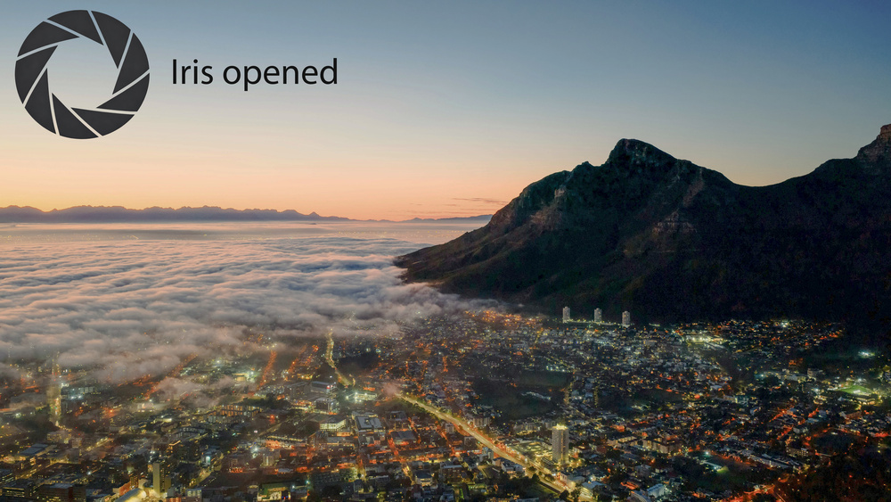 A panoramic shot of Cape Town at dusk, with an overlay indicating the projector's iris is open. The black levels in dark areas are raised, and the overall contrast is low.