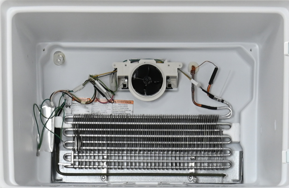 This exposed evaporator sits at the back of the freezer section at the top of the refrigerator. It consists of a silver tube folded back on itself eight times, surrounded by metal fins. There's a fan on top. There are electrical connections running to the fan, the heater and a temperature sensor taped to the evaporator refrigerant inlet capillary tube.