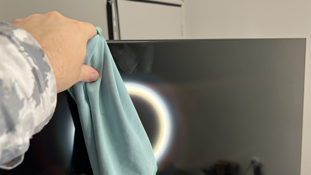 Someone using a microfiber cloth to clean smudges from a TV screen.