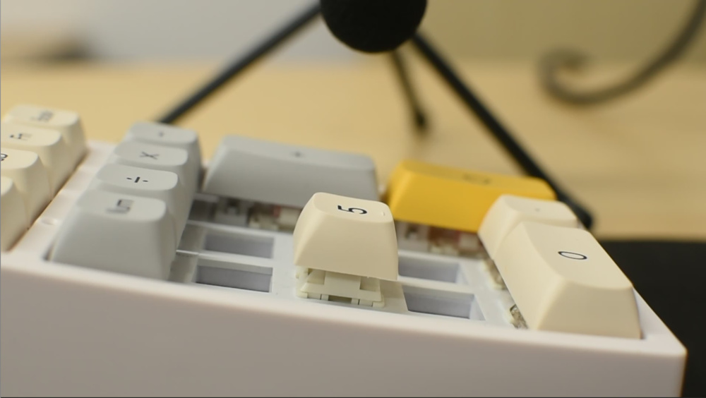 A close-up shot of a macropad with several switches removed and a microphone positioned above for sound recording.