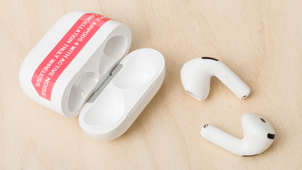 An open case for the Apple AirPods 4 With Active Noise Cancellation, and the earbuds are shown outside of the case on a light wood surface.