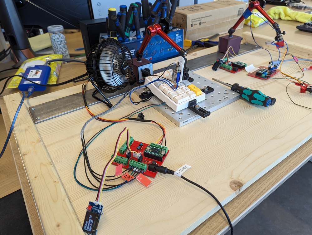 Keyboard switch testbench with a hot-swappable macropad, solenoid actuator on an articulating arm, custom breadboard, and USB analyzer for latency testing.