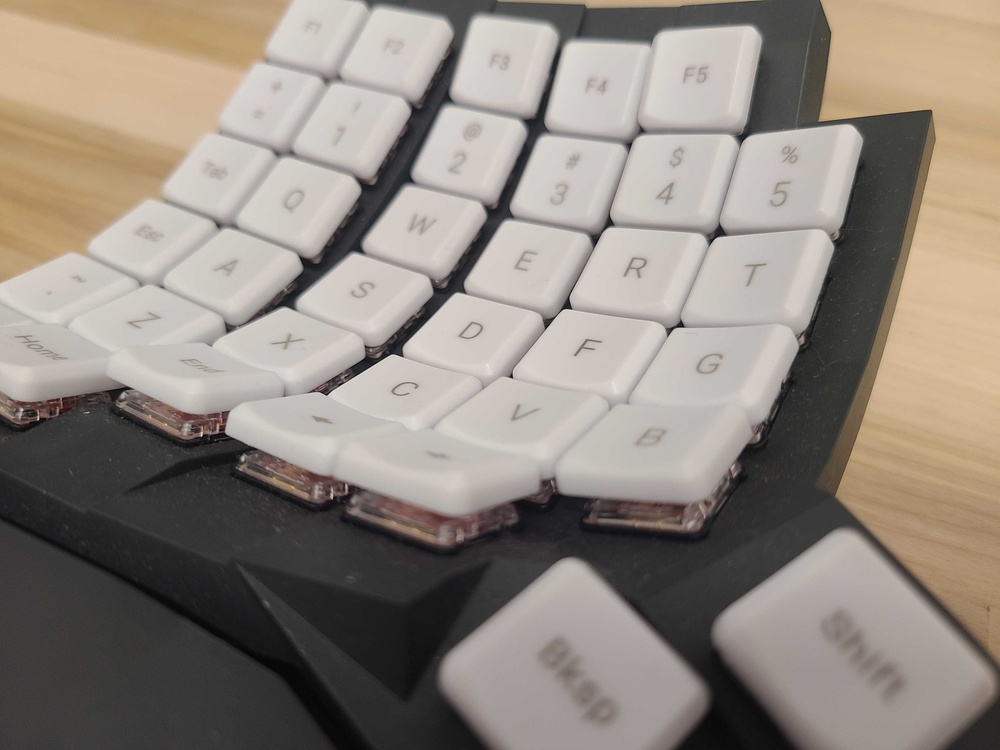 A close-up angled view of the MoErgo Glove80 keyboard, showing its smooth white POM keycaps with a slightly curved ergonomic layout and a glossy, almost slippery-looking surface.