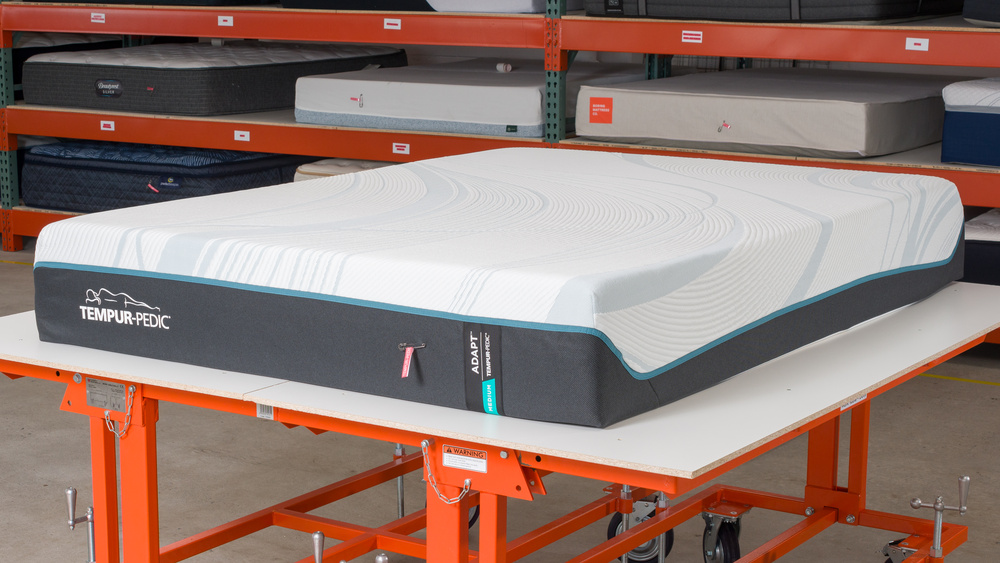 The Tempur-Pedic TEMPUR-Adapt, a foam mattress, in front of a range of other mattresses in an industrial setting.