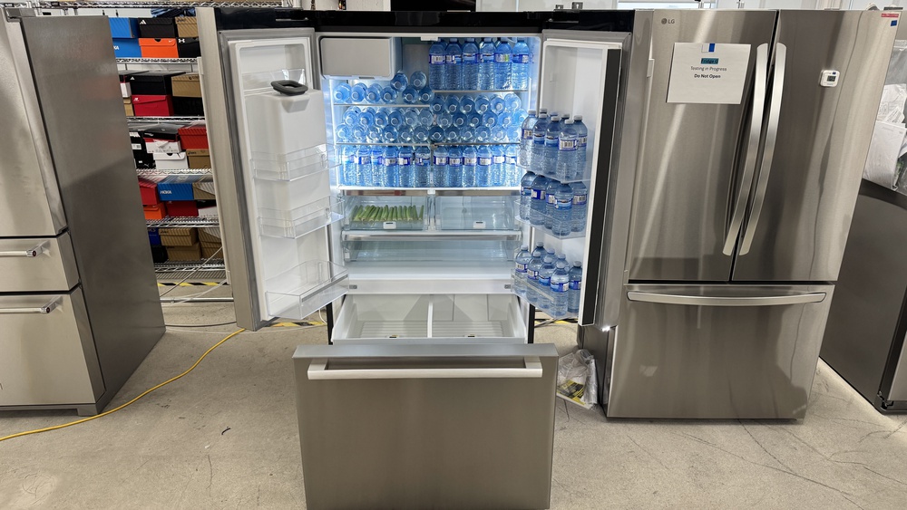 A French door refrigerator with its doors open and the freezer pull-out drawer extended out. The fridge doors don't extend out very wide but the freezer drawer front extends out a lot further, a fair distance from the back of the refrigerator.
