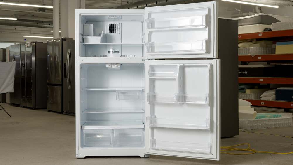 The all-white interior of a top freezer refrigerator. In the refrigerator section, there are three shelves, a cheese or deli drawer on the bottom right of the upper shelf, and two pull-out crisper drawers on the bottom. with both doors open. In the door is an enclosed butter bin, two half-width adjustable height bins, and two full-width bins. The bottom bin is shallow to clear the crisper drawers inside the fridge.