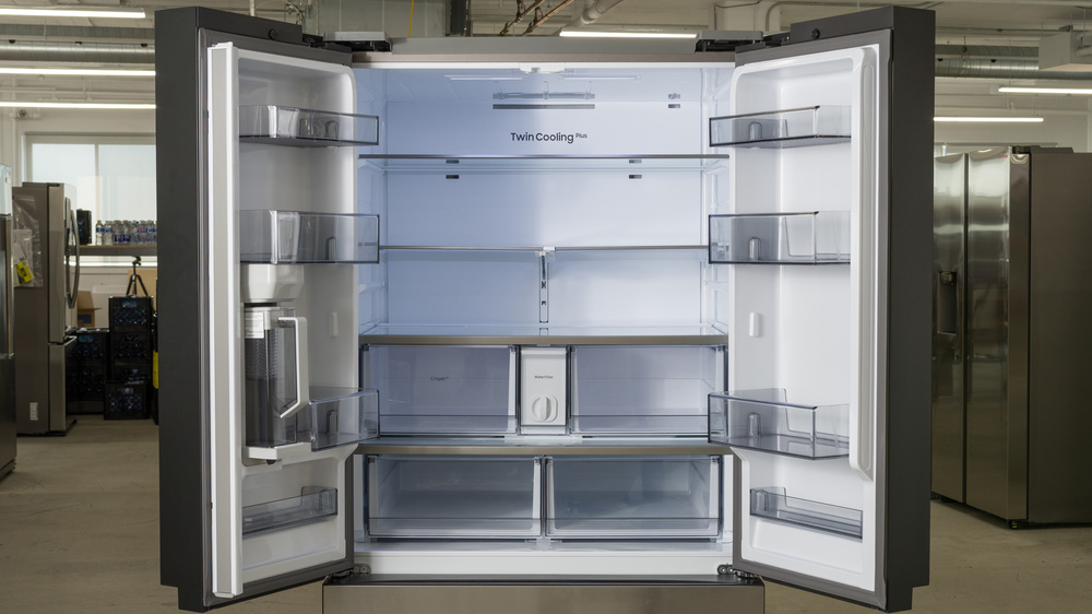 The interior of the refrigerator of a French door fridge. The door on the left has two full-width bins, a water pitcher with a partial-width bin beside it, and a shallow bottom bin. The central section of the compartment contains three glass shelves, with two shallow crisper drawers underneath and two deep crisper drawers on the bottom. There's a water filter housing between the two shallow crisper drawers. The door on the right contains a short bin at the top, two tall bins, and a shallow bin at the bottom.