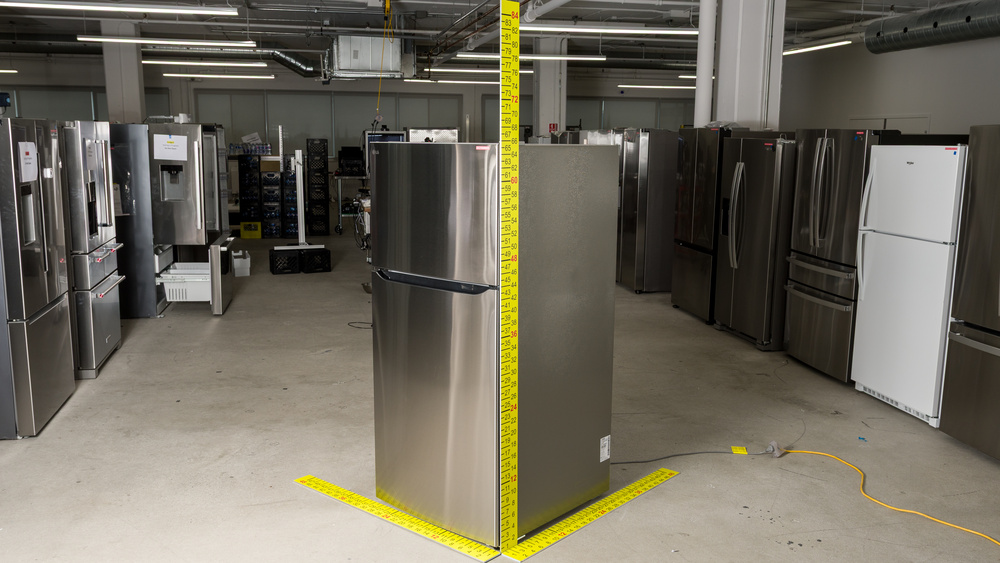 A stainless steel refrigerator with dimensioned sticks positioned to measure width, depth and height. Width is 30", depth is between 33" and 34", and height is almost 66".