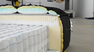 A close-up of the Beautyrest Black mattress in a warehouse-like environment, cross-sectioned to show the different layers inside.