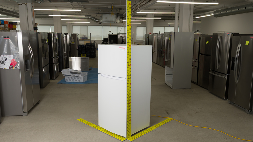 A white refrigerator with dimensioned sticks positioned to measure width, depth and height. Width is between 27" and 28", depth is 29", and height is 60".