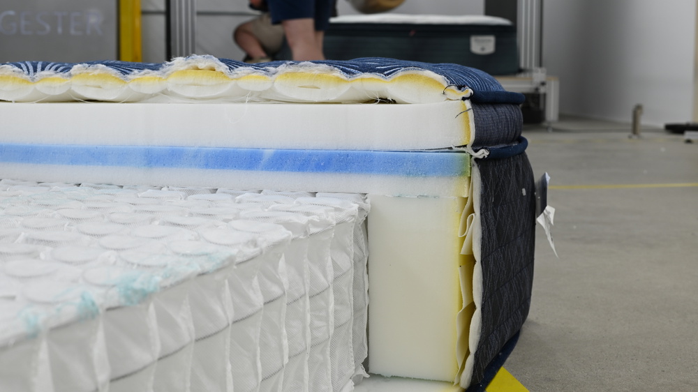 A close-up of the edge component of the Serta Perfect Sleeper Innerspring mattress; it's in a warehouse-like location and you can see people working in the background.