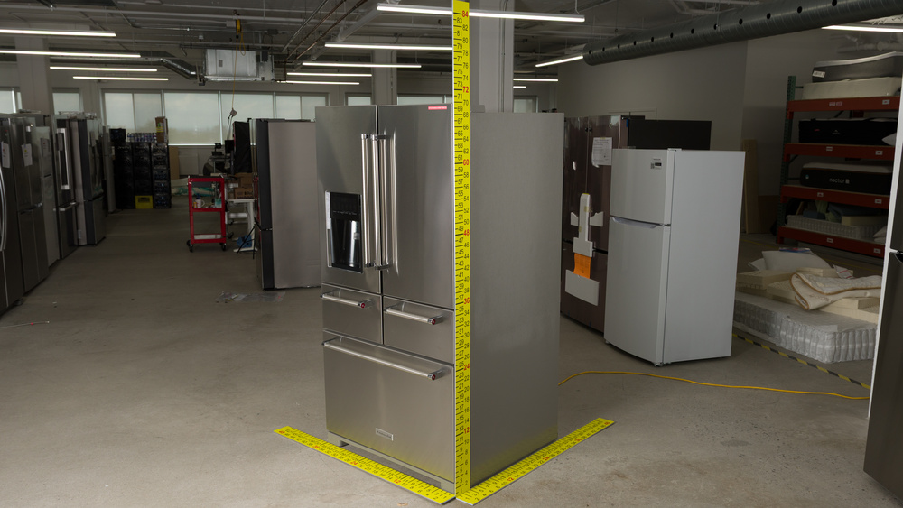 A stainless steel refrigerator with dimensioned sticks positioned to measure width, depth and height. Width is 36", depth is 36", and height is 70".