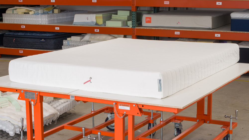 The Sleep on Latex Pure Green Organic in front of a range of other mattresses in an industrial setting.