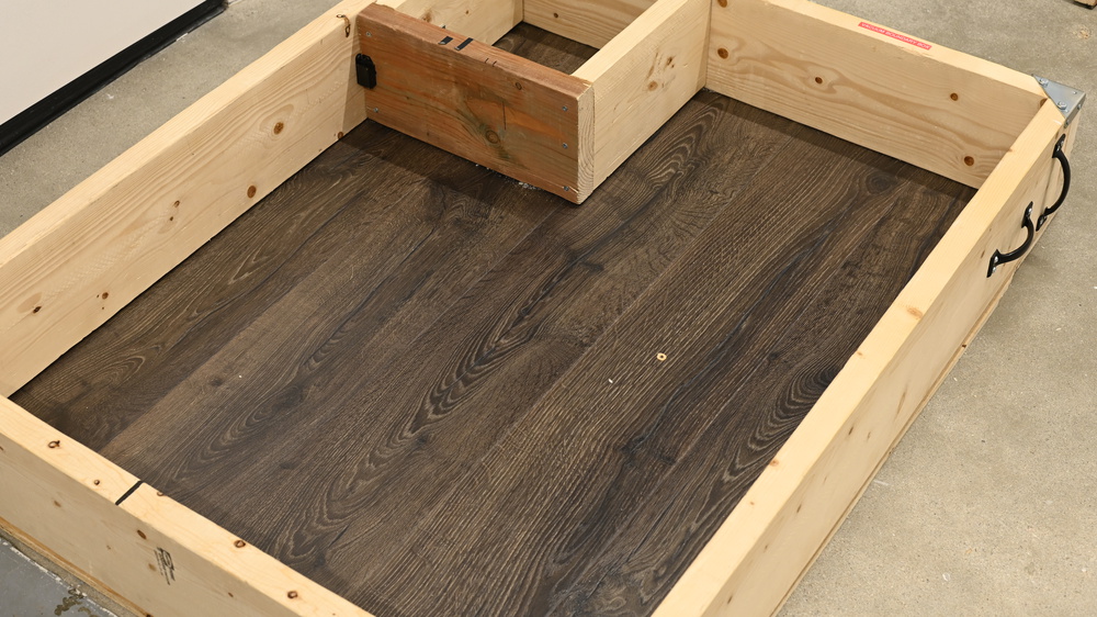 A nearly completely bare floor inside a wooden bounding box. There's a single piece of cereal and one piece of rice remaining.