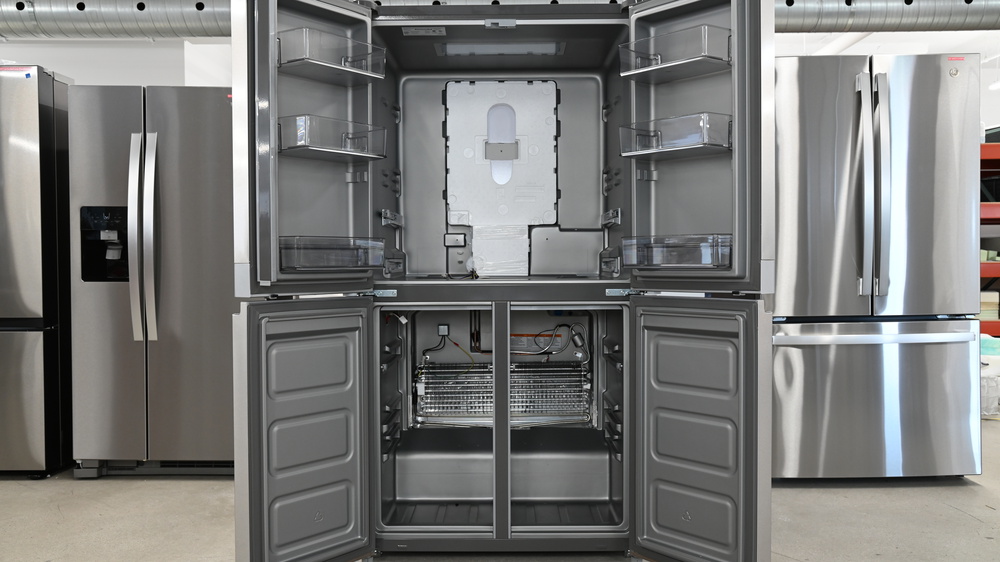 The gray interior of a 4-door fridge. All shelves, drawers, and panel covers have been removed. There's a wide silver evaporator in the rear of the lower freezer section.