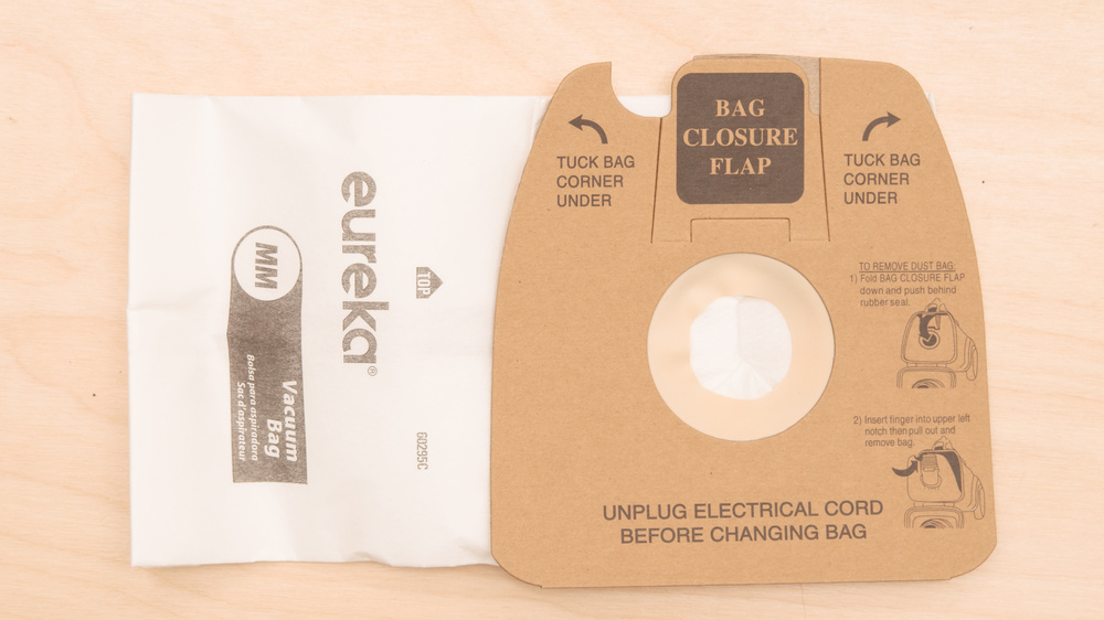 A white Eureka filter bag with a cardboard seating surface. At the top of the cardboard, there's a cutout labeled "BAG CLOSURE FLAP." Instructions below indicate to fold the flap down and push it behind the rubber seal. The rubber seal surrounds the inlet hole in the center of the cardboard.