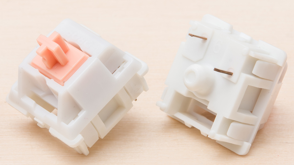 Close-up of two 2-pin mechanical switches shown from different angles, with white housings and a pink stem.