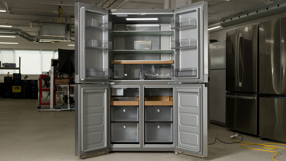 The interior of a 4-door refrigerator. There are three door bins in the left door of the refrigerator section on top, with a shallow bottom bin. There are three glass shelves in the fridge with two crisper drawers mounted underneath the third shelf. The door on the right has three door bins, with the bottom bin shallow to clear the crisper drawers inside the fridge. The freezer section underneath has plain double doors with no bins, and there are two freezer compartments, with an ice maker and ice tray in the upper left, then a medium-height pull-out bin and a tall pull-out bin. On the right, there's a short pull-out tray with a medium height pull-out bin, then a tall pull-out bin at the bottom.